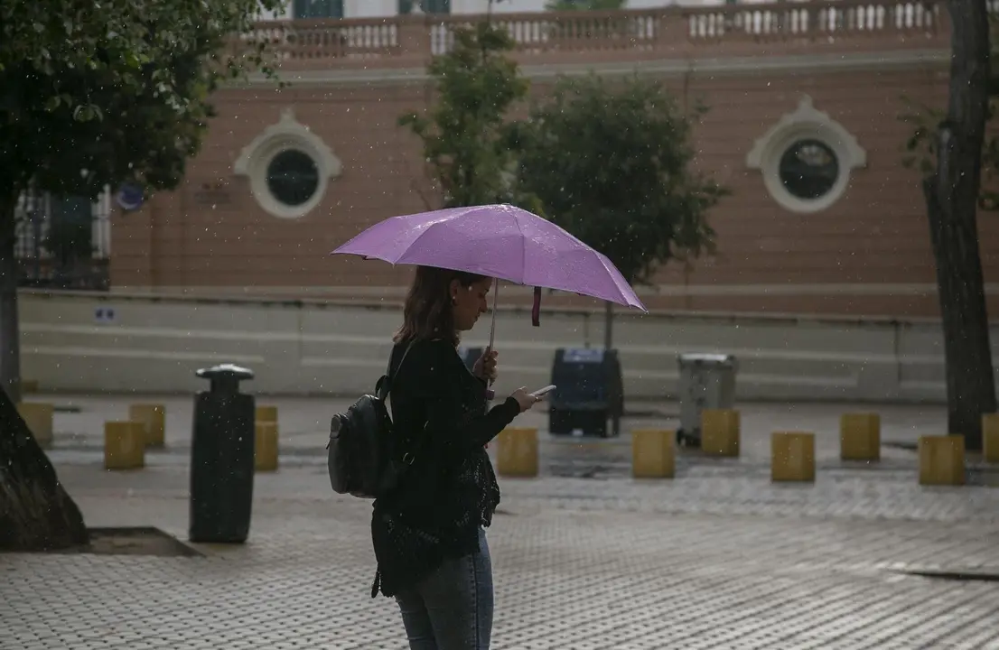 Una mujer se protege de la lluvia bajo su parag&uuml;as mientras camina. Sevilla.