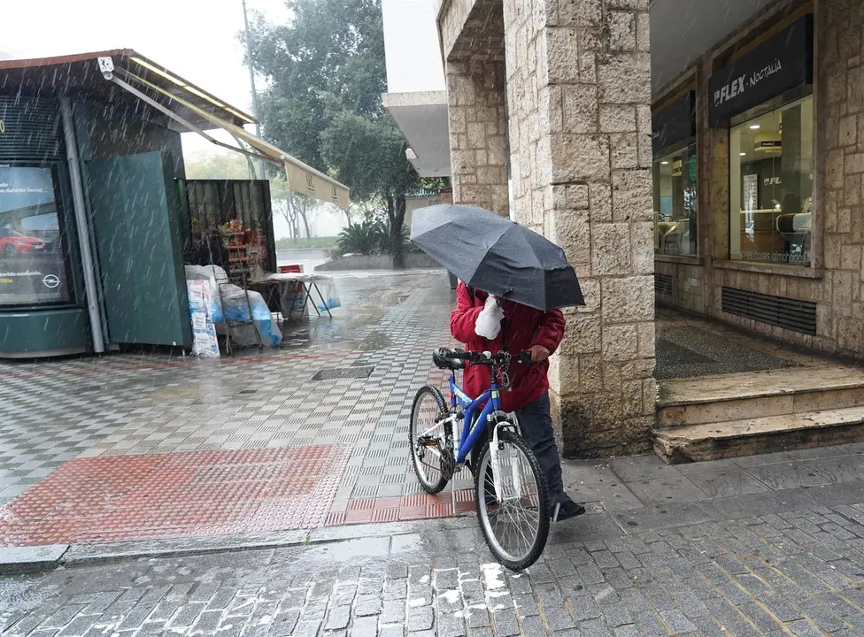 Un ciclista con un pagaguas resguard&aacute;ndose de la lluvia y el viento