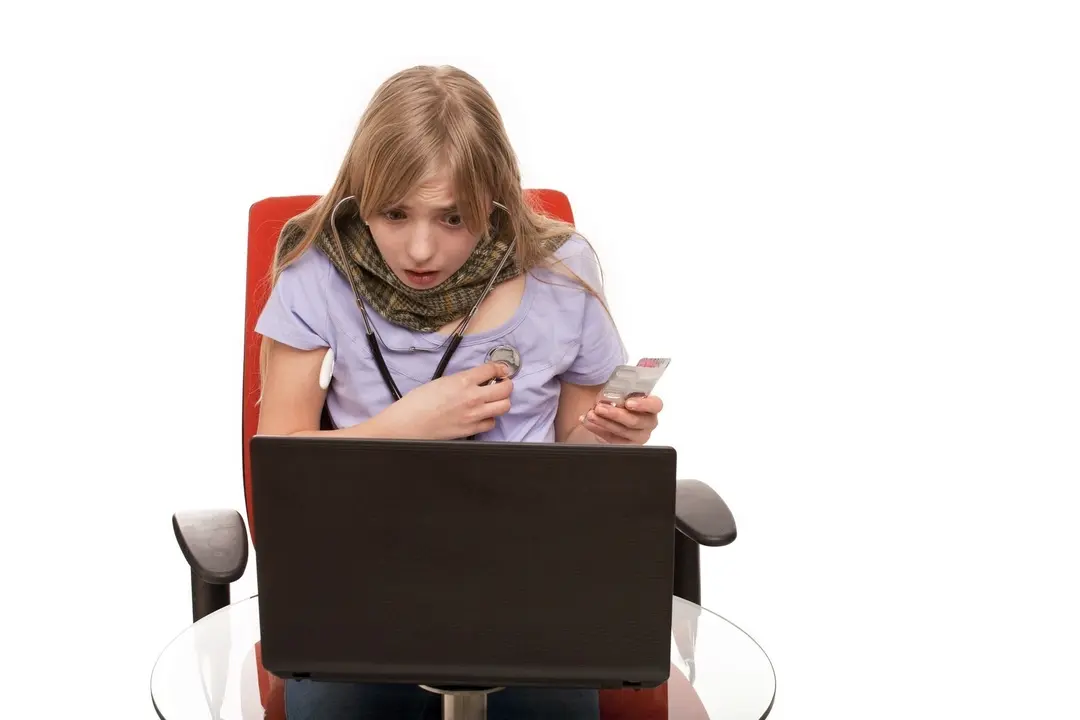Hypochondria - Young Female checking herself with a stethoscope and searching information about her disease on a laptop.