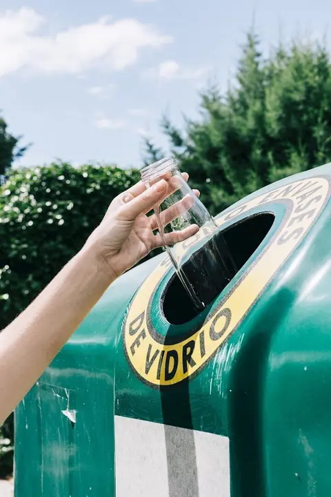 Una mujer reciclando un residuo de envase de vidrio en el contenedor verde