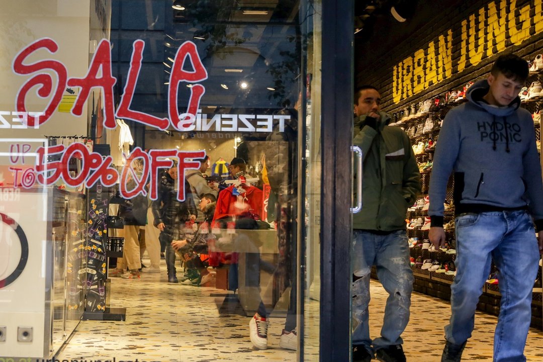Dos hombres salen de una tienda de zapatos en Madrid, donde se ofertan rebajas de hasta el 50%.