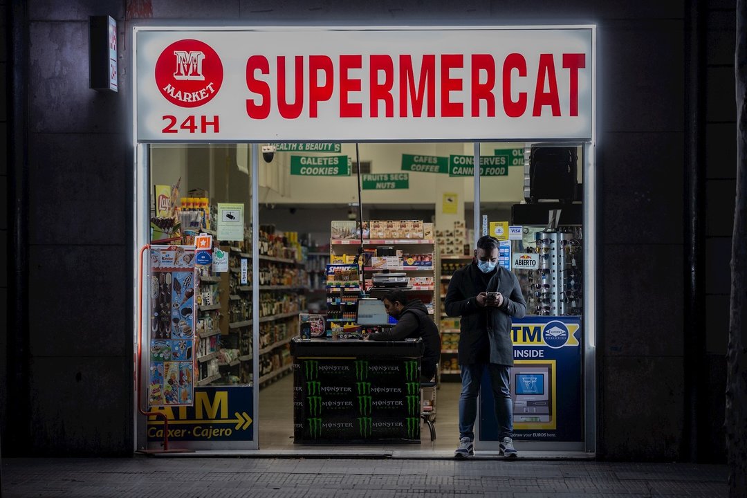 Un hombre protegido con una mascarilla en la puerta de un supermercado 24 horas abierto durante el primer día laborable de la segunda semana desde que se decretó el estado de alarma en el país a consecuencia del coronavirus, en Barcelona/Catalunya (España