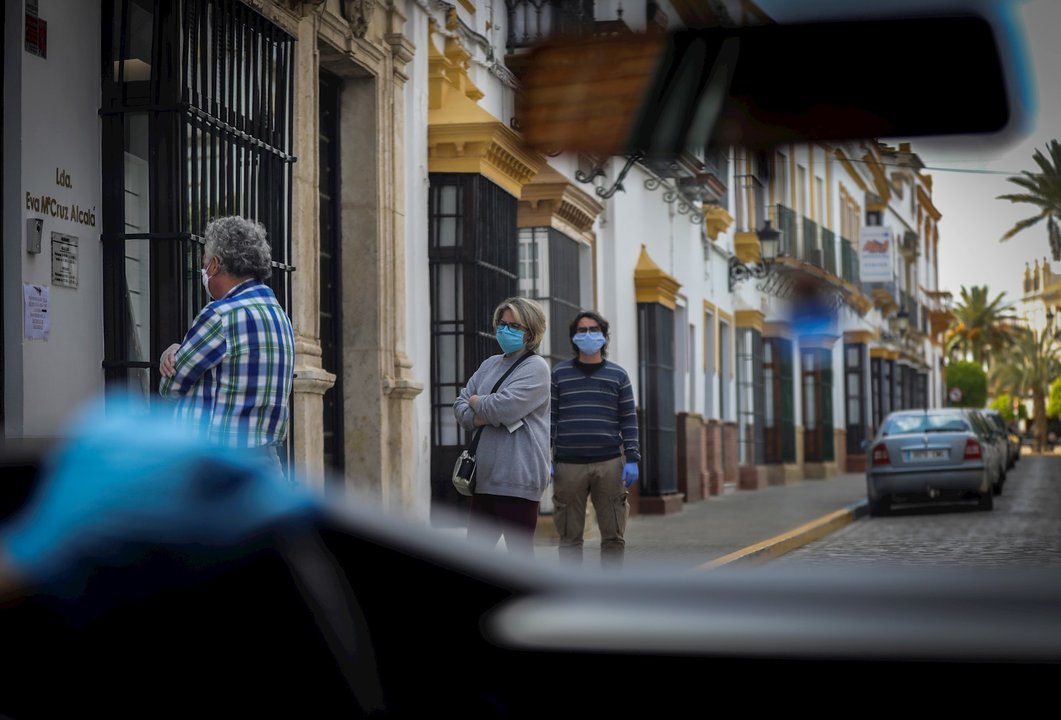 Personas hacen cola para acceder al banco durante el período de confinamiento en el estado de alarma por coronavirus, covid-19. En Arahal, Sevilla (Andalucía, España), a 25 de marzo de 2020.