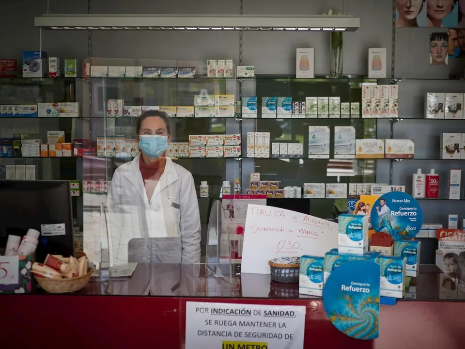Una farmac&eacute;utica contin&uacute;a trabajando protegida por una m&aacute;scara sanitaria y una mampara.
