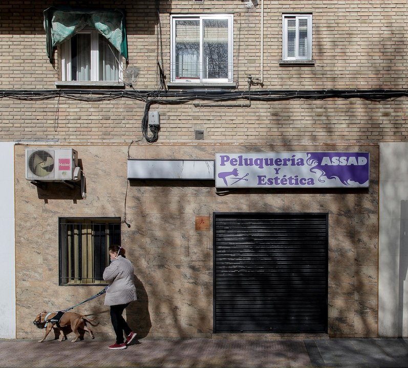 Una mujer pasea a un perro cerca de una peluquería cerrada durante el primer día laborable desde que se decretó el estado de alarma en todo el territorio nacional a consecuencia del coronavirus, en Alcorcón (Madrid), a 16 de marzo de 2020.