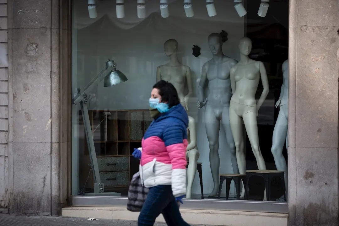 Una mujer protegida con una mascarilla pasa junto a un escaparate de una tienda cerrada durante el noveno d&iacute;a laborable desde que se decret&oacute; el estado de alarma en el pa&iacute;s a consecuencia del coronavirus, en Barcelona/Catalunya (Espa&ntilde;a) .