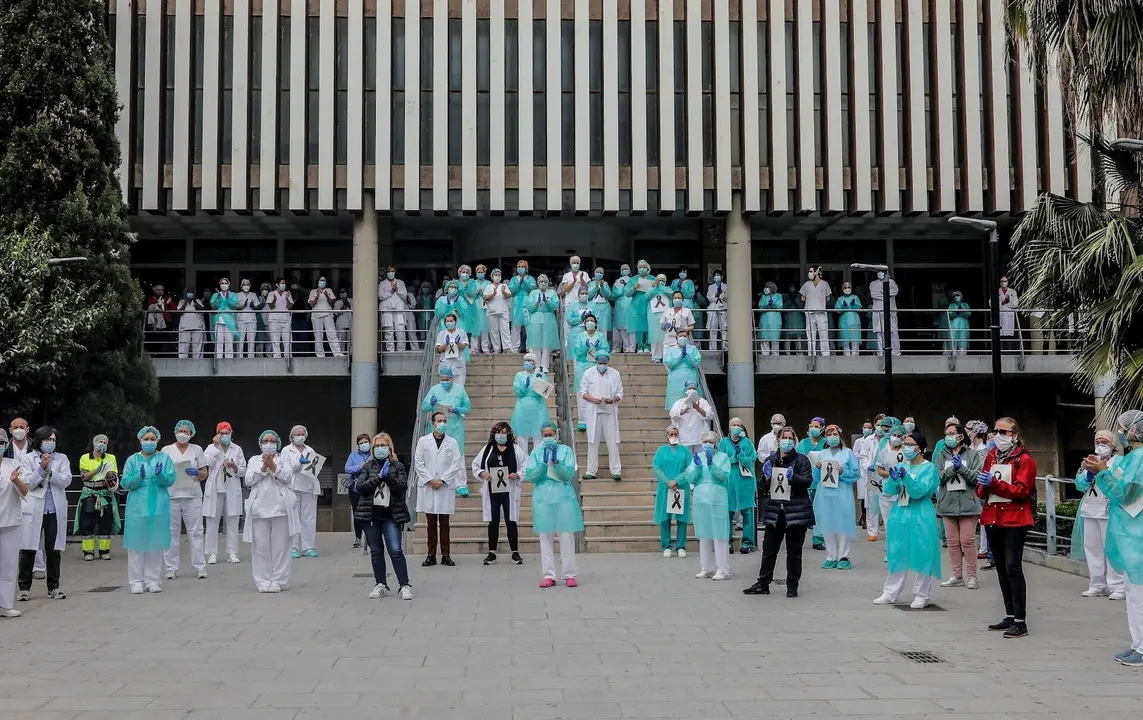 Sanitarios protegidos con mascarillas aplauden conmocionados tras el minuto de silencio en la entrada del Hospital Doctor Peset por la t&eacute;cnica de enfermer&iacute;a fallecida por coronavirus, en Valencia/Comunidad Valenciana (Espa&ntilde;a) a 6 de abril de 2020.