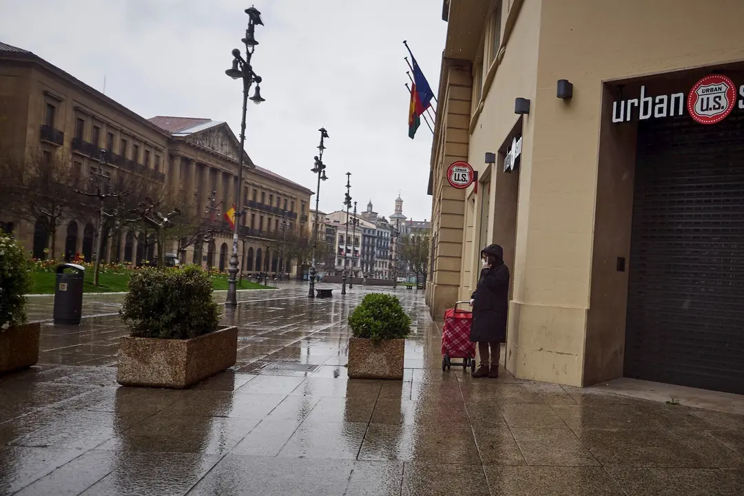 Una mujer camina bajo la lluvia con el carro de la compra frente al Palacio del Gobierno de Navarra durante el Martes Santo y la cuarta semana del estado de alarma decretado por el Gobierno por la crisis del coronavirus, en Pamplona/Navarra (Espa&ntilde;a) a 7 d