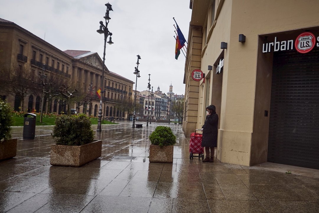 Una mujer camina bajo la lluvia con el carro de la compra frente al Palacio del Gobierno de Navarra durante el Martes Santo y la cuarta semana del estado de alarma decretado por el Gobierno por la crisis del coronavirus, en Pamplona/Navarra (España) a 7 d