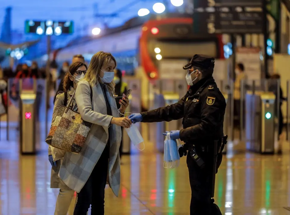 Un polic&iacute;a nacional entrega una mascarilla a una mujer en el vest&iacute;bulo de la estaci&oacute;n del Norte de Valencia el d&iacute;a en el que se reactiva la actividad laboral no esencial en las empresas cuyos empleados no puedan teletrabajar