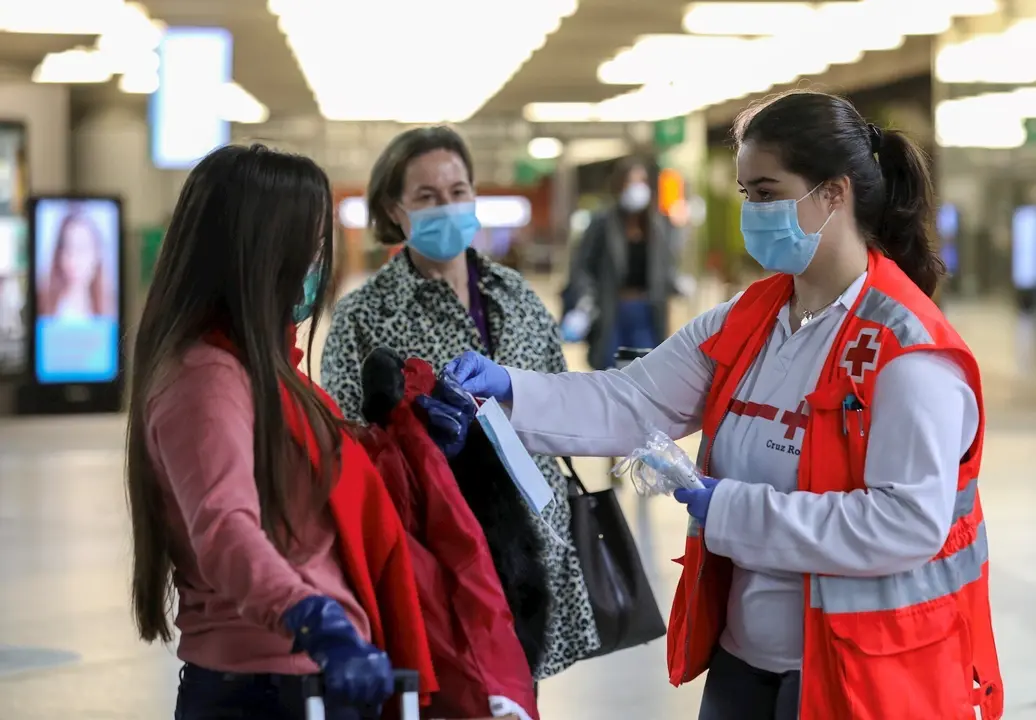 Voluntarios de Cruz Roja entregan mascarillas a pasajeros en la estaci&oacute;n de Cercan&iacute;as de Atocha, en Madrid