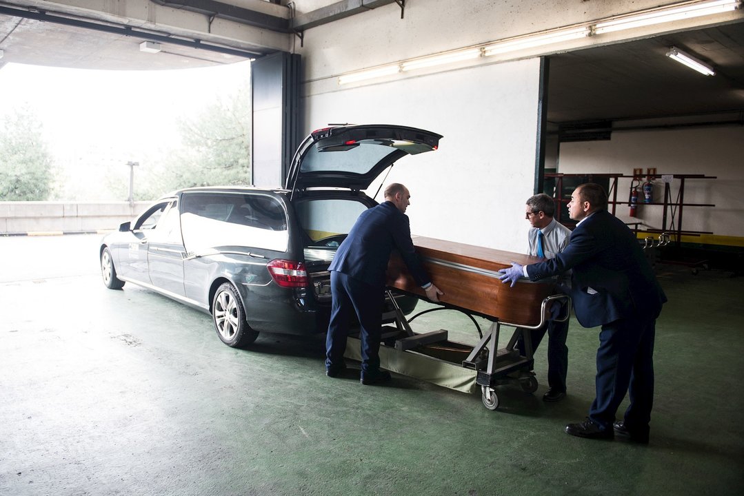 Trabajadores de servicios funerarios introducen un féretro en el vehículo 