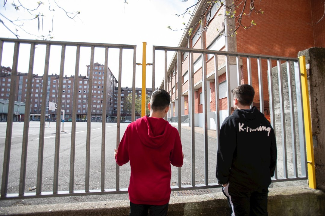 Dos adolescentes observan el patio cerrado de un colegio durante el confinamiento por el Estado de Alarma