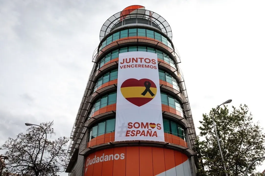 Ciudadanos despliega una lona con un cresp&oacute;n negro junto a la bandera de Espa&ntilde;a en su sede nacional.