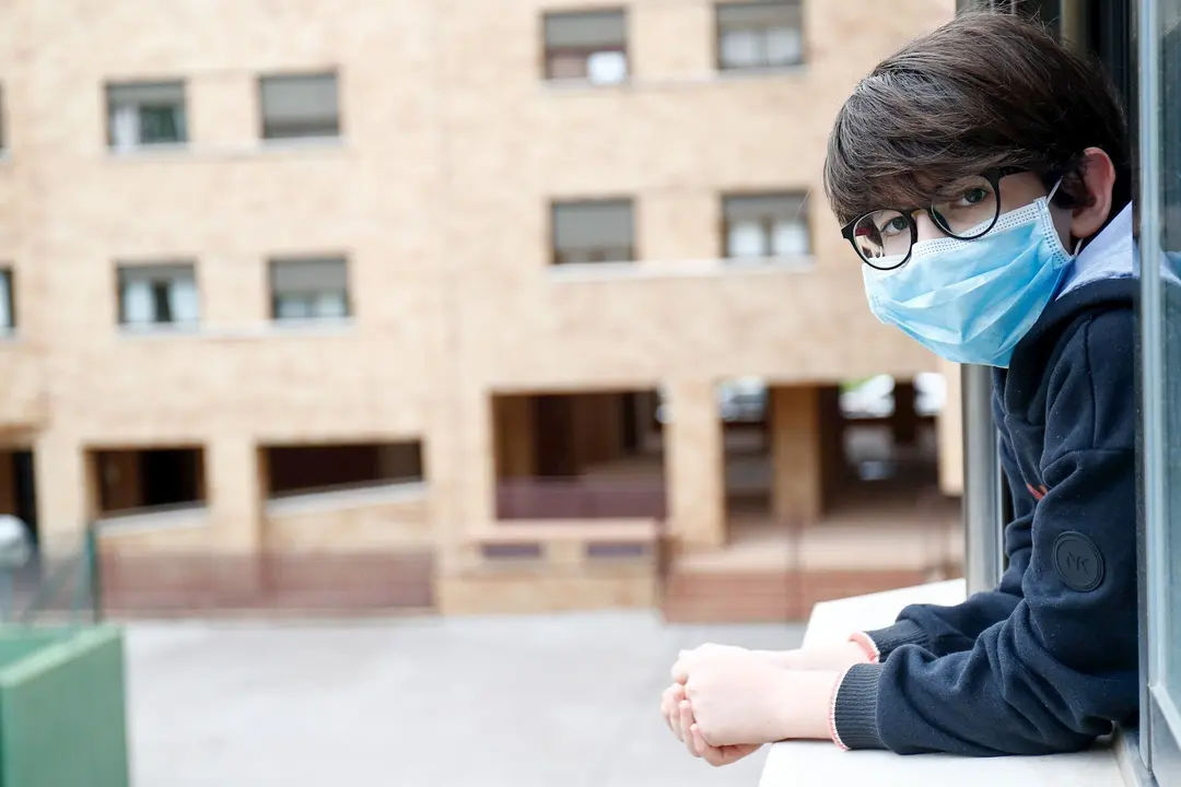 Un ni&ntilde;o con una mascarilla se asoma a la ventana de su casa de Valdemoro (Madrid) durante el confinamiento.