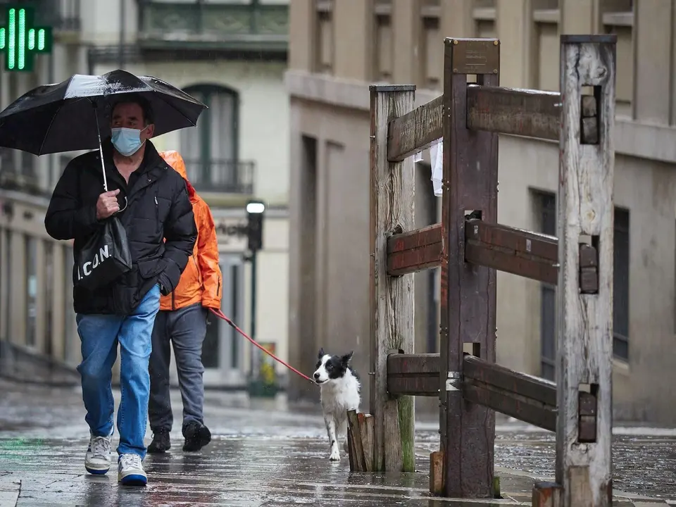 Un hombre con mascarilla camina bajo la lluvia junto al vallado permanente del encierro de Pamplona de la cuesta de Santo Domingo