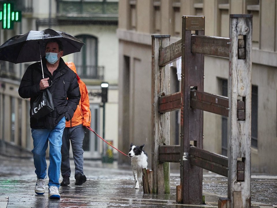 Un hombre con mascarilla camina bajo la lluvia junto al vallado permanente del encierro de Pamplona de la cuesta de Santo Domingo
