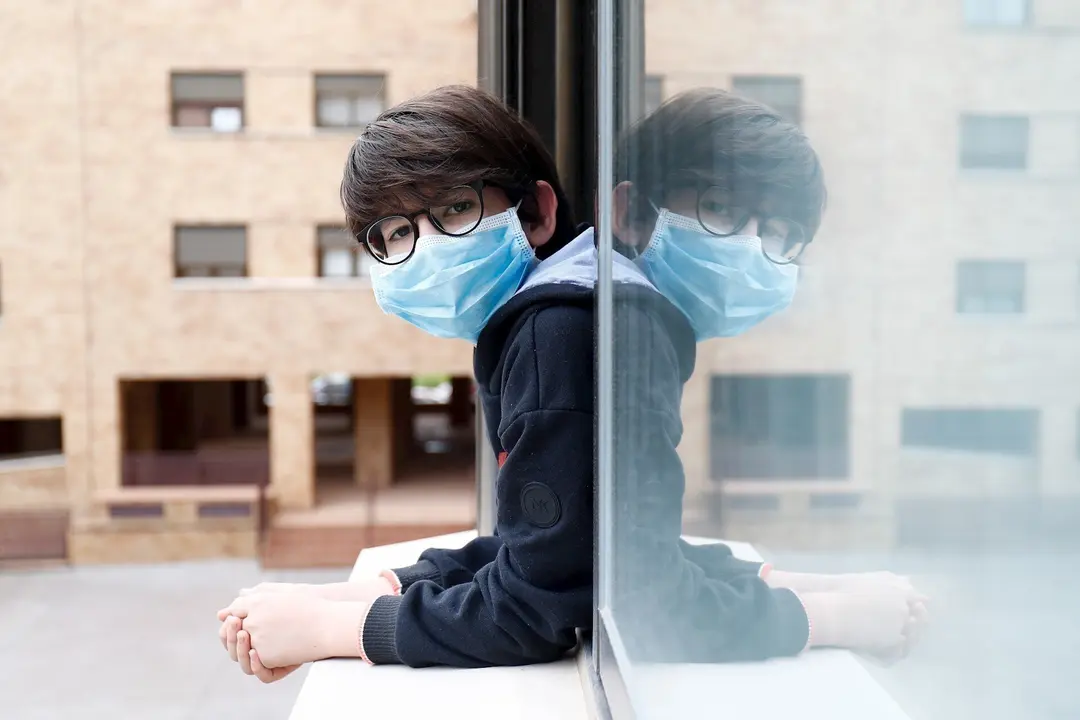 Un ni&ntilde;o con una mascarilla se asoma a la ventana de su casa durante el confinamiento por el coronavirus, en Valdemoro/Madrid (Espa&ntilde;a) a 20 de abril de 2020.