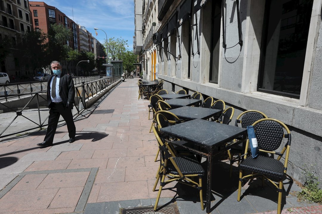 Un hombre con mascarilla pasa junto a una terraza cerrada de un bar 
