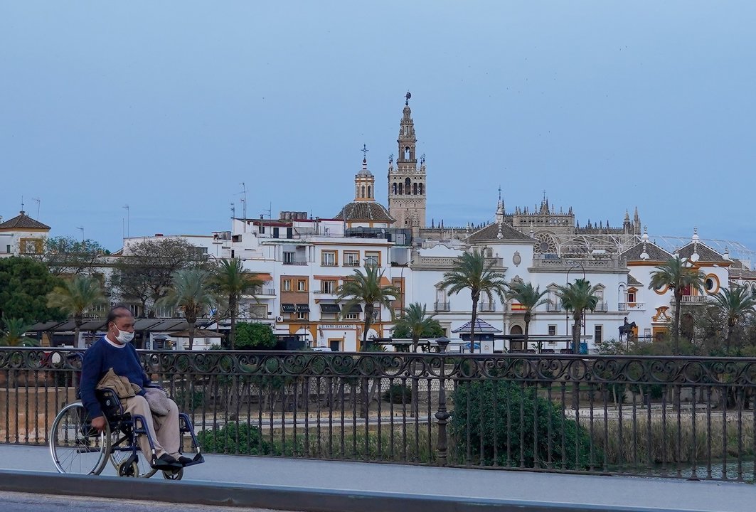 Un ciudadano en silla de ruedas por el Puente de Triana casi desértico a los 40 días de estado de alarma en Sevilla a 23 abril del 2020