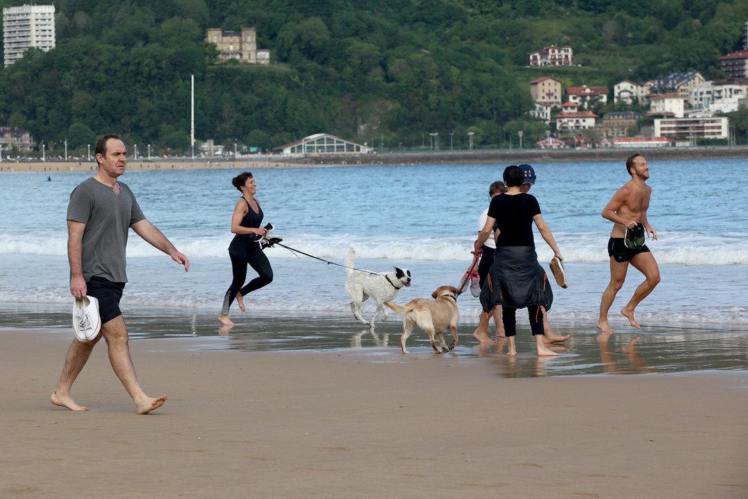 Varias persona caminan y corren con perros en la playa de La Concha en el día en que el Gobierno permite salir a hacer deporte de forma individual y pasear con otra persona con la que se conviva. En San Sebastián / Guipúzcoa (España), a 2 de mayo de 2020.