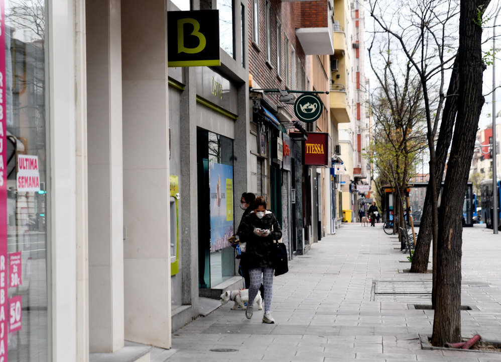 Una mujer con mascarilla espera su turno frente a una sucursal de Bankia