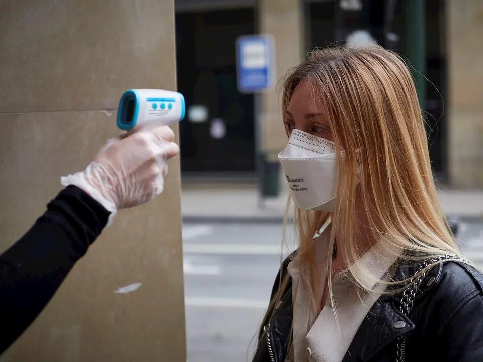 Una trabajadora de la tienda de moda Urban Sons le toma la temperatura a una clienta