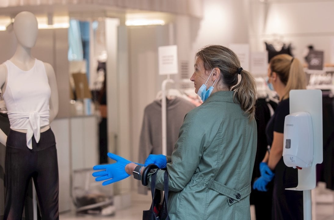 Una mujer se coloca unos guantes proporcionados por el establecimiento al entrar en una tienda de ropa. durante el segundo día de la fase 1 del plan de desescalada que ha elaborado el Gobierno de España. 