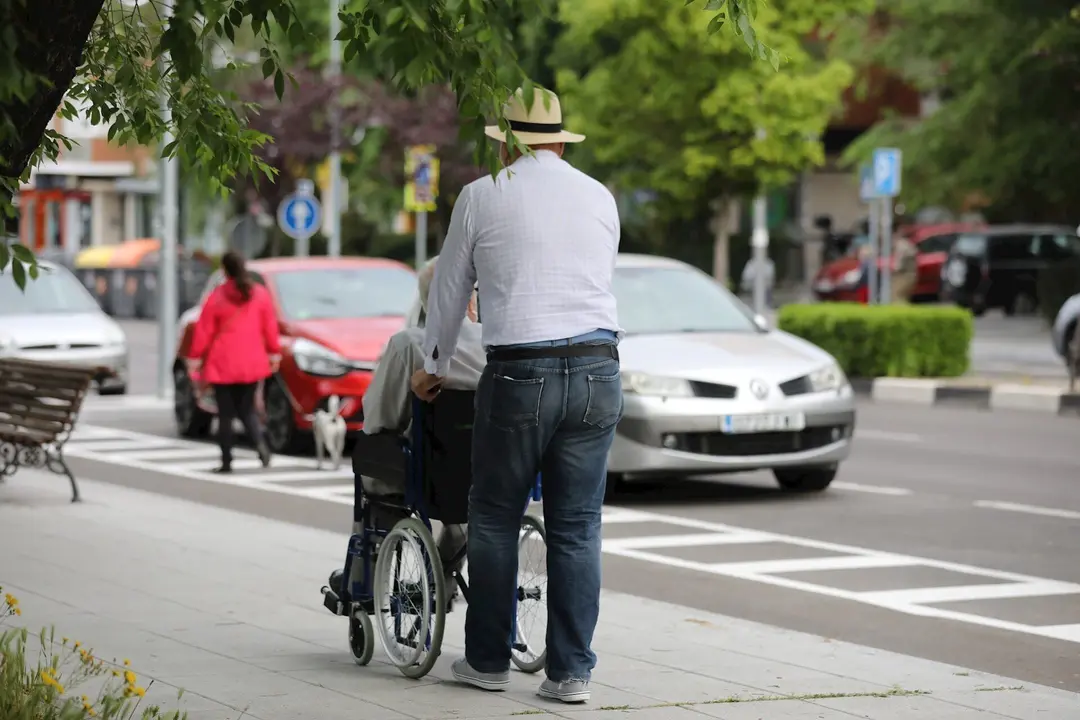 Un hombre pasea a una persona de edad avanzada en silla de ruedas durante su franja horaria permitida en la desescalada por la crisis del Covid-19 donde aquellos mayores de 70 a&ntilde;os pueden salir a la v&iacute;a p&uacute;blica de 10.00 a 12.00 horas y de 19.00 a 20.00 ho