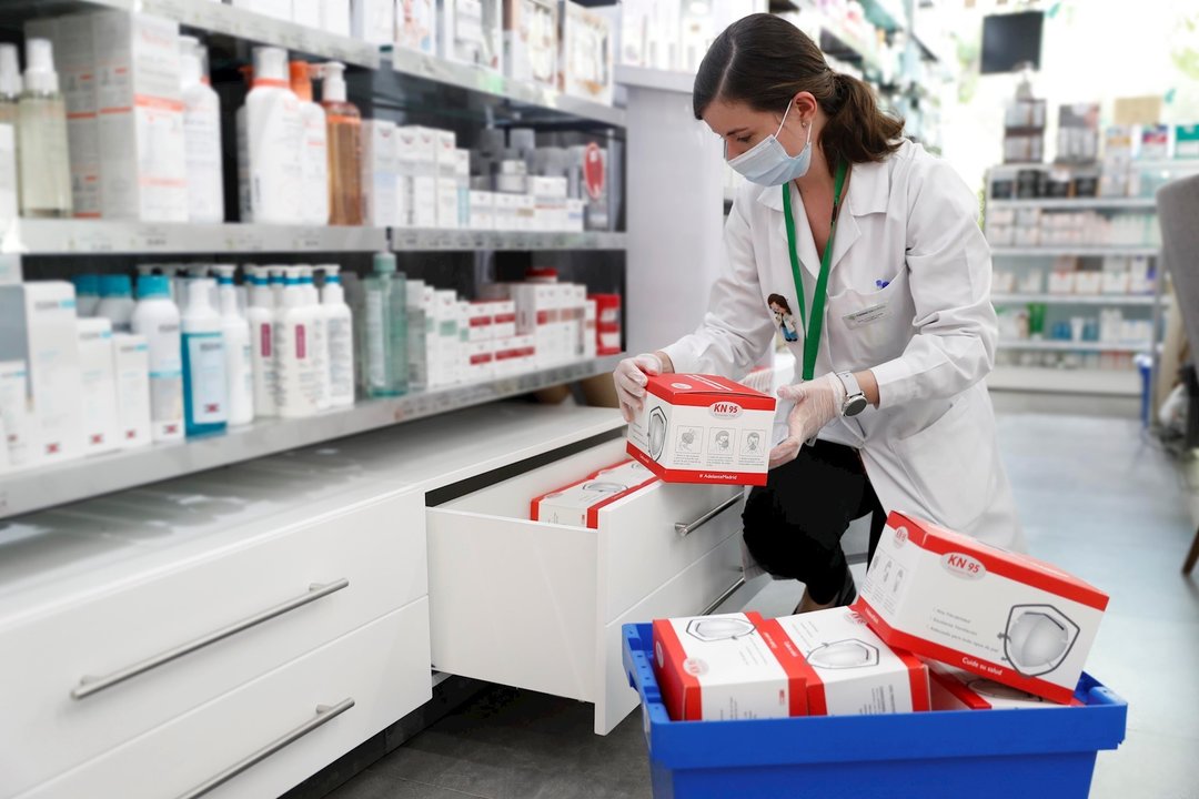 Una farmacéutica coloca cajas con mascarillas.