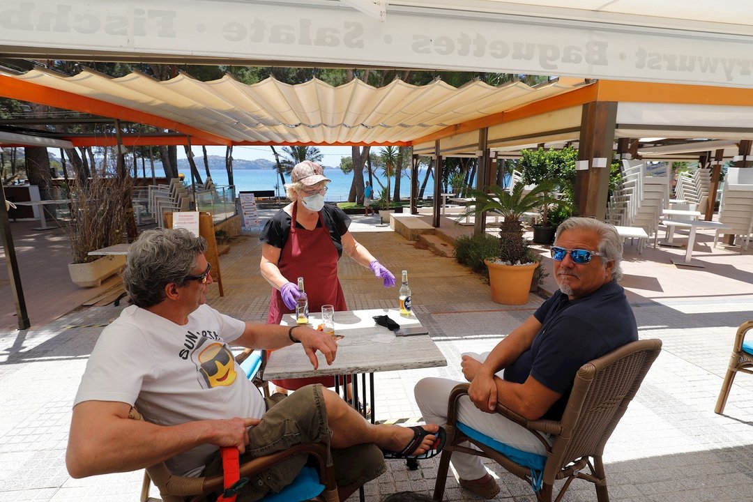 20 May 2020, Spain, Calvia: A waitress serves beer to customers at the "Essbar" restaurant terrace on the beach of Paguera on the Spanish island of Mallorca. Some Spanish provinces have been allowed to relax the first blocking measures in a first phase si