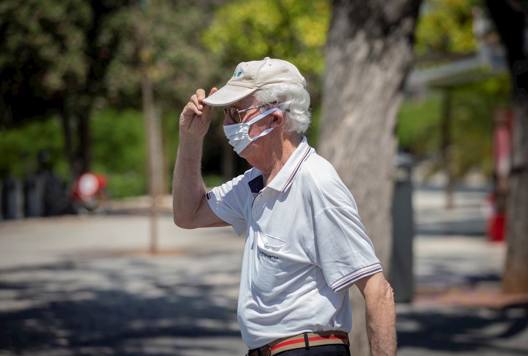 Un hombre con mascarilla y gafas de sol se coloca una gorra