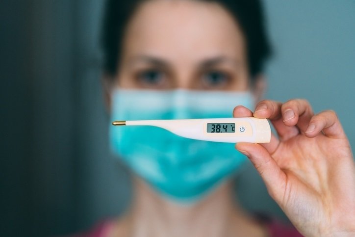 Imagen de recurso de una mujer con un termómetro y mascarilla.