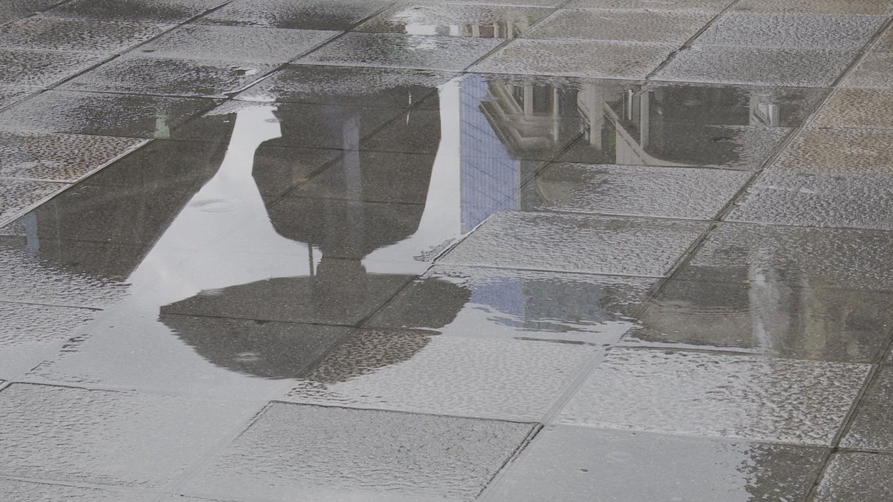 Una persona con paraguas se refleja en un charco provocado por la lluvia