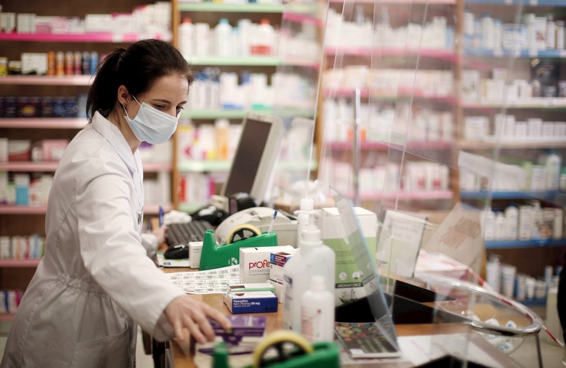 Una farmacéutica con mascarilla despacha en una farmacia. 