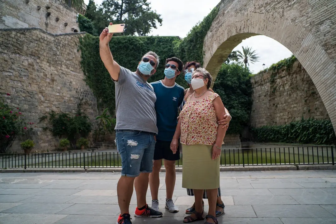 Varios turistas se hacen una foto junto a los Jardines de S'Hort del Rei de Palma de Mallorca durante el primer d&iacute;a de uso obligatorio de la mascarilla en Baleares por el Covid-19, en Palma de Mallorca, Islas Baleares (Espa&ntilde;a) a 13 de julio de 2020. 