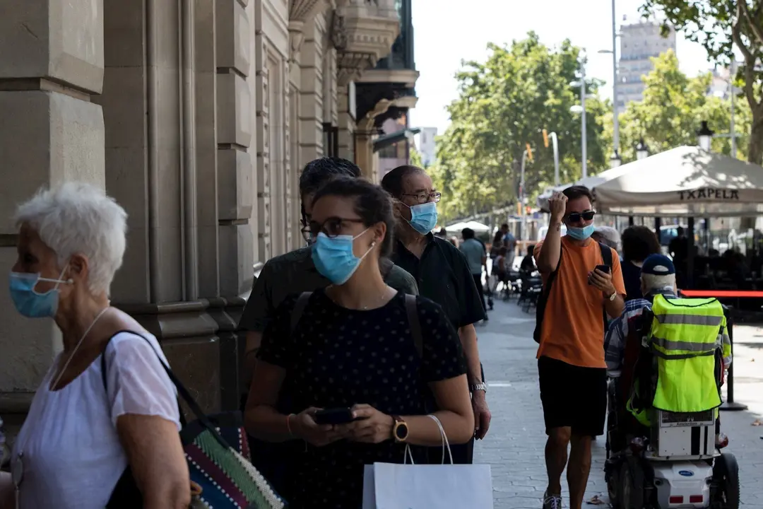 Decenas de personas protegidas con mascarilla hacen cola para entrar en una biblioteca, en Barcelona, Catalunya (Espa&ntilde;a), a 23 de julio de 2020.