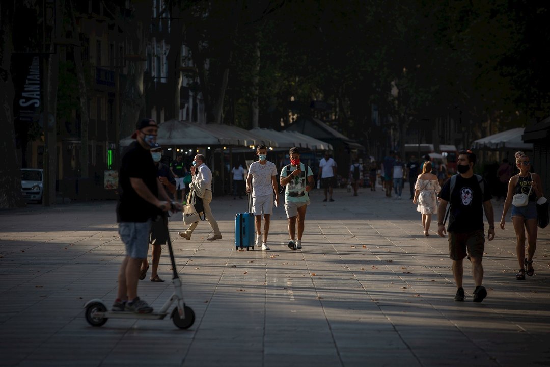 Dos jóvenes caminan, uno de ellos lleva una maleta, en Barcelona, Catalunya (España), a 28 de julio de 2020.