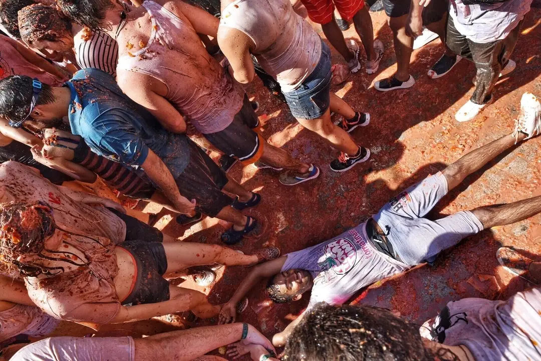Un joven se tumba en el suelo cubierto con los restos de los tomates arrojados durante la fiesta de la Tomatina de Bu&ntilde;ol 2019.