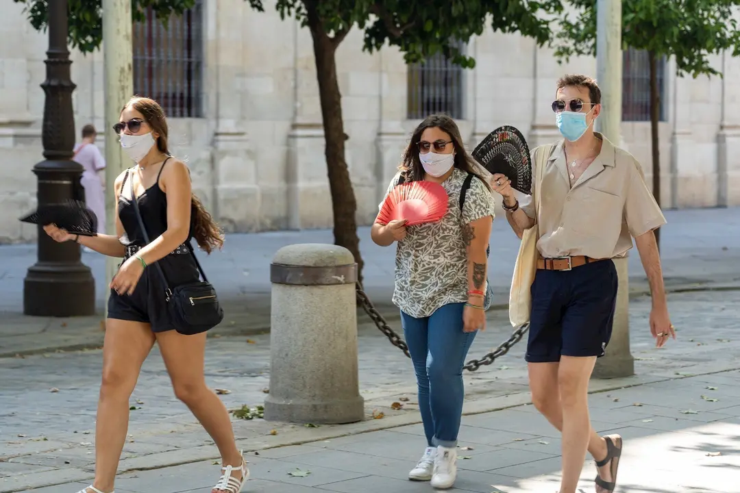 Tres j&oacute;venes pasean con mascarillas y  abanico en el primer d&iacute;a  de uso obligatorio de mascarillas en Sevilla a 15 de julio del 2020