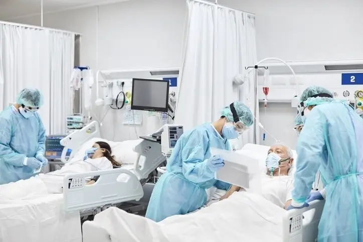 Doctors and nurses taking care of patients in ICU. Team of frontline coworkers are treating man and woman. They are at hospital during COVID-19. (Doctors and nurses taking care of patients in ICU. Team of frontline coworkers are treating man and woman