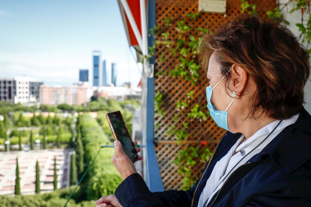 Araceli, usuaria de audífonos intracanales y miembro de FIAPAS, observa su teléfono móvil desde un balcón. En Madrid (España) a 12 de junio de 2020.