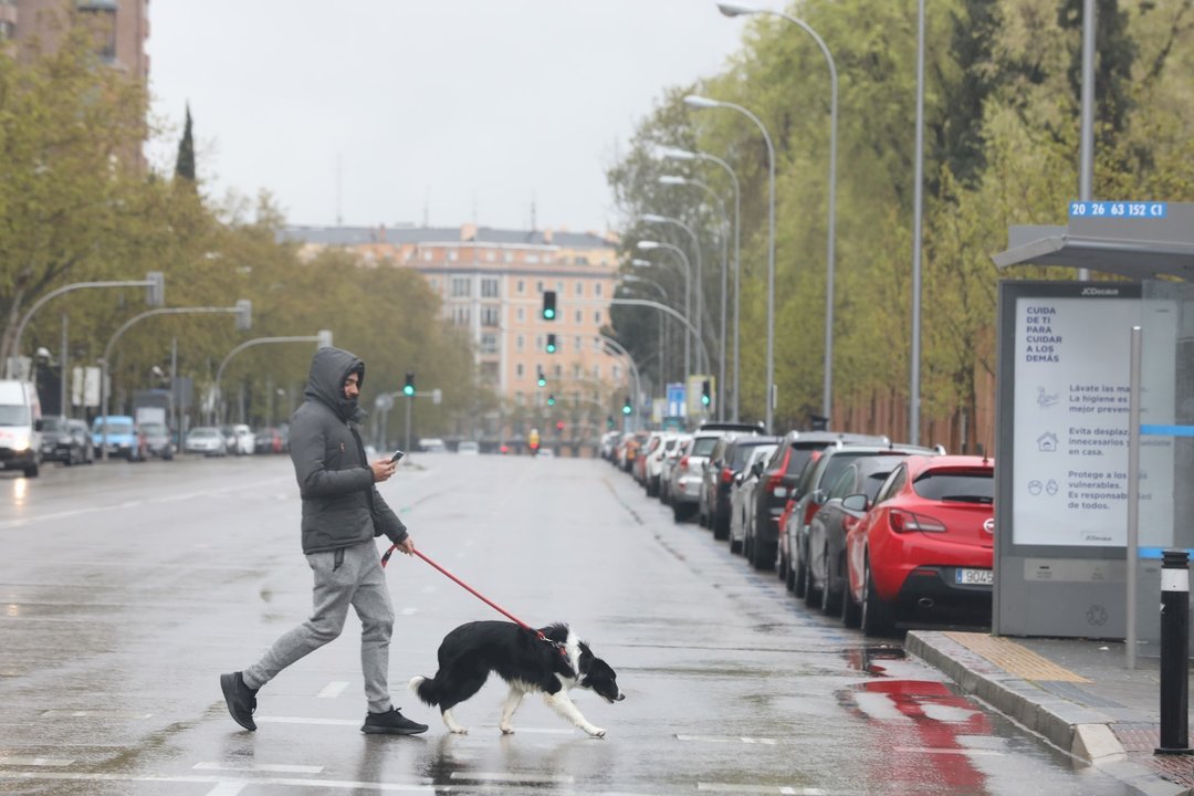 Un joven pasea un perro por el centro de la capital donde las temperaturas han bajado estrepitosamente durante el segundo día de la entrada en vigor de la limitación total de movimientos salvo de los trabajadores de actividades esenciales, medida adoptada
