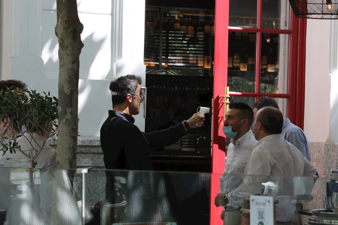 Un camarero mide la temperatura de sus clientes en una céntrica terraza madrileña en el primer día de la Fase 1, cuando se reabren al público las terrazas al aire libre de los establecimientos de hostelería y restauración limitándose al 50% de las mesas y