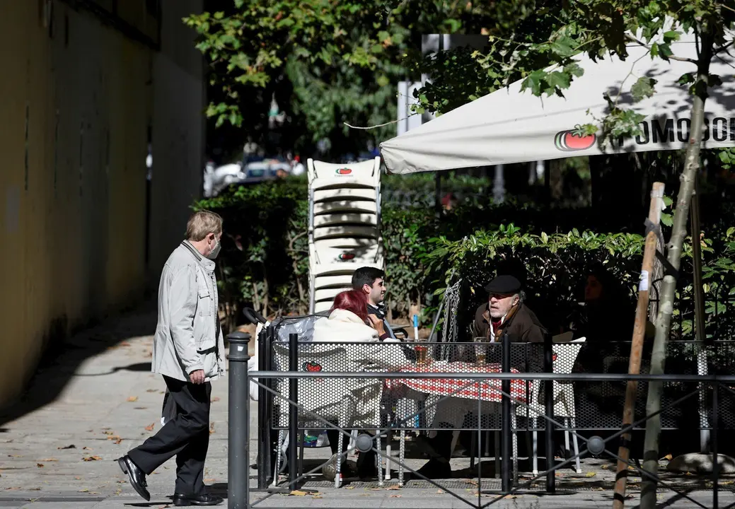 Un hombre camina frente a la terraza de un bar donde hay sentadas otras tres personas en la zona b&aacute;sica de salud de Guzm&aacute;n el Bueno, en el distrito de Chamber&iacute;, en Madrid (Espa&ntilde;a), a 26 de octubre de 2020. Guzm&aacute;n el Bueno es una de las zonas b&aacute;sicas de sa