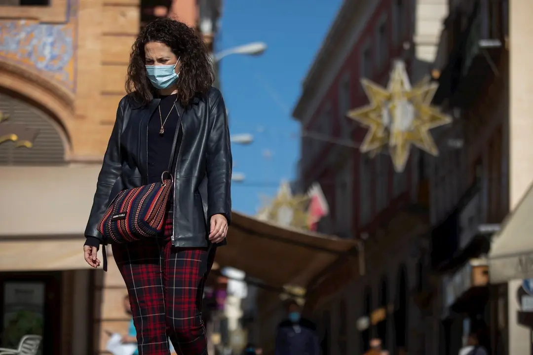 Una mujer con mascarilla camina por la plaza de San Francisco, al fondo las luces del alumbrado de navidad de la calle Sierpes, en Sevilla (Andaluc&iacute;a, Espa&ntilde;a), a 20 de noviembre de 2020.