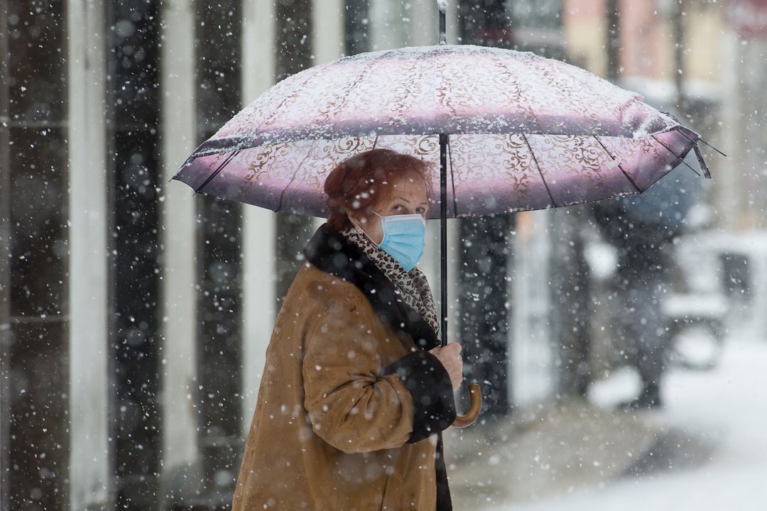 Una mujer se cubre de la nieve con un paraguas en Becerrea, en Lugo, Galicia (España), a 4 de diciembre de 2020. Hoy se ha producido la primera gran nevada del otoño en la montaña lucense. La intensa nevada que está cayendo sobre el centro de la provincia