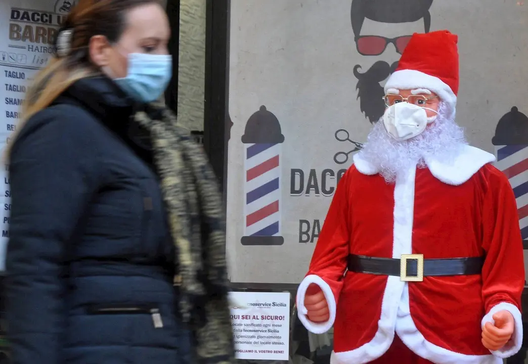 Una mujer con mascarilla pasando junto a un Pap&aacute; Noel con mascarilla en Palermo, Sicilia, Italia