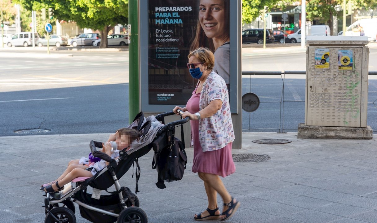 Una señora con mascarillas pasea a dos niños ante un cartel publicitario en el primer día  de uso obligatorio de mascarillas en Sevilla a 15 de julio del 2020