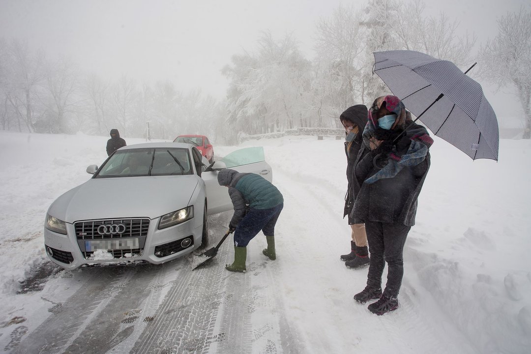 Varias personas limpian la carretera con una pala para ayudar a un coche atrapado en la nieve 
